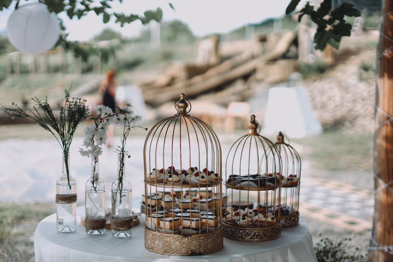Beautiful outdoor garden party setup with decorative cakes in birdcages and floral accents on a table.